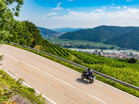 Waldviertel © Alexander Seger Motorrijder op kronkelende landweg met wijngaarden en rivier op de achtergrond