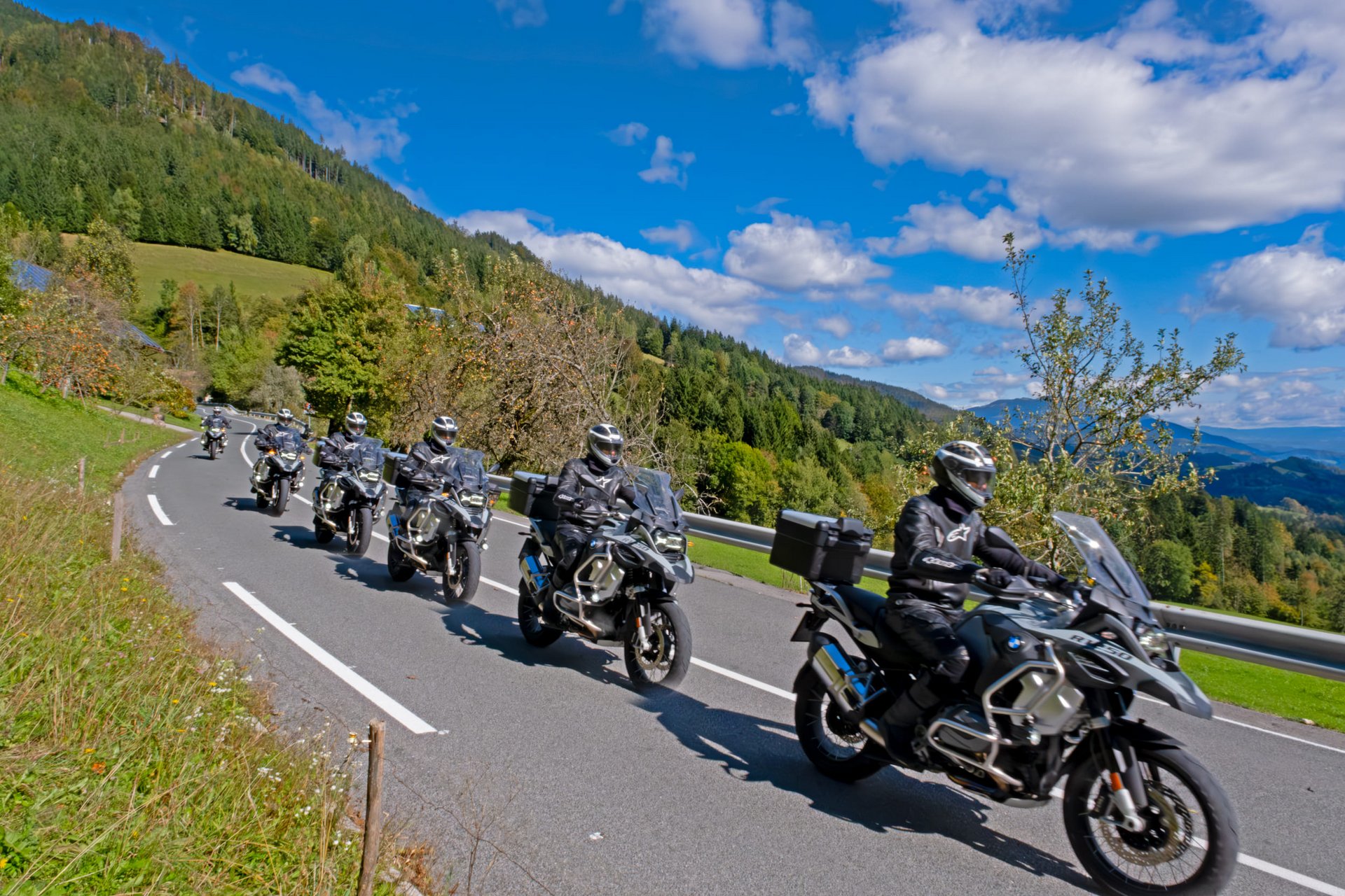 Motorvakantie © Igor Rosina Groep motorrijders op landelijke weg met beboste heuvels en blauwe lucht