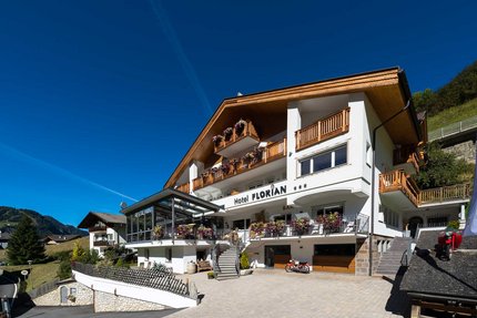Hotel Florian © Arik Oberrauch Hotel Florian met houten balkons en bloemen onder een heldere blauwe lucht