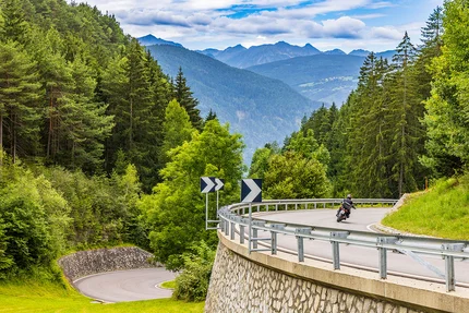Südtirol - Dolomiten © Alexander Seger Motorradfahrer fährt auf kurviger Bergstraße im Wald