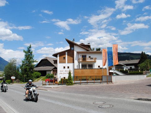 MOAR'S Hotel © Moar's Hotel in Olang Motorradfahrer fahren an einem Hotel in den Bergen bei sonnigem Wetter vorbei