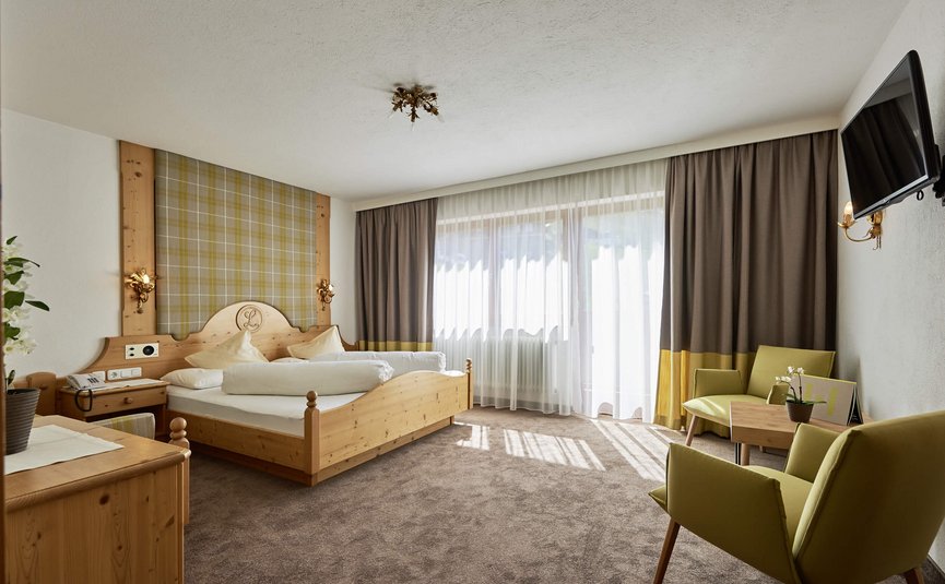 Alpenhotel Laurin ***S © studio22.at - Marcel Hagen Helles Hotelzimmer mit Holzbetten, zwei Stühlen und TV an der Wand