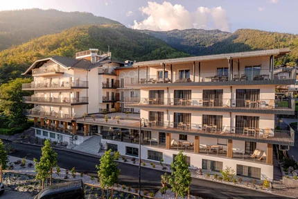 Cristallo Sport & Wellness Hotel © Andrea Acler Modern hotelgebouw met balkons voor beboste berg in zonlicht