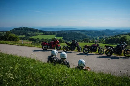 Niederösterreich © Moppetfoto.de Drei Motorradfahrer sitzen am Straßenrand mit Blick auf grüne Hügel und blaue Berge