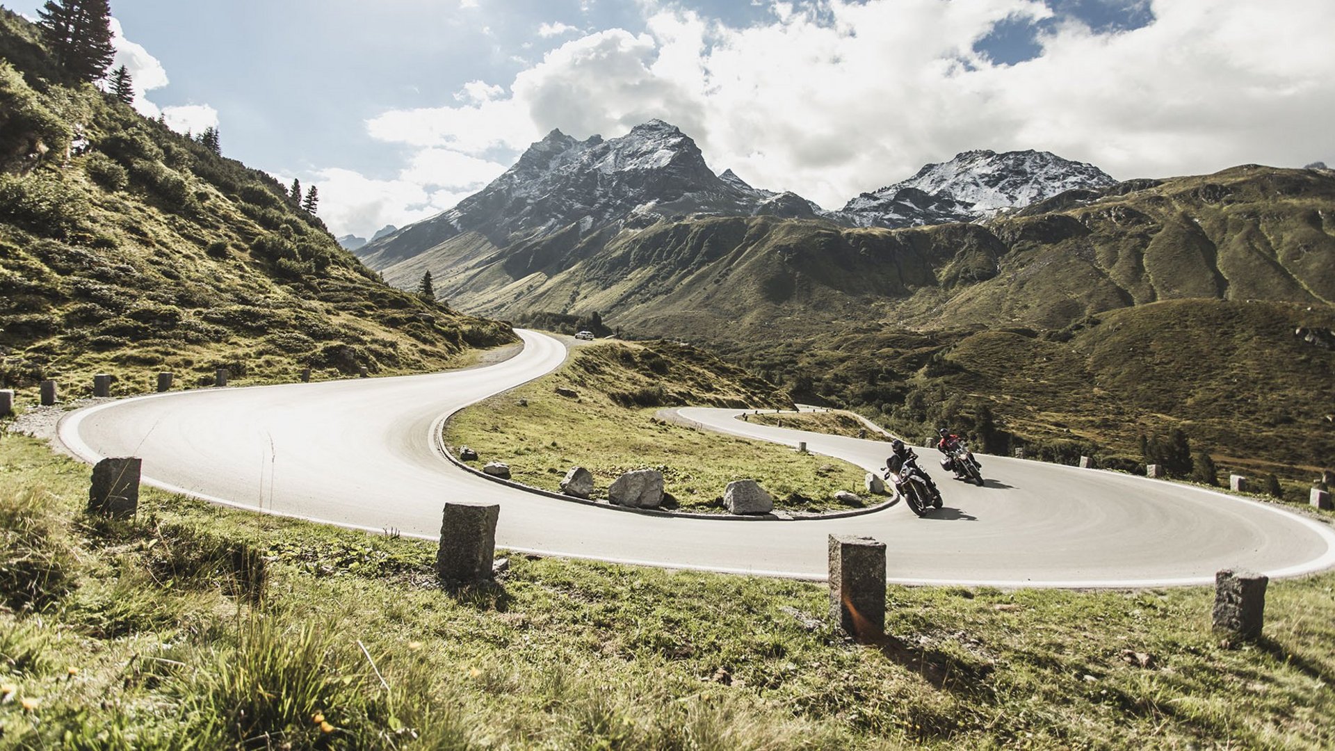 Newsletter © Christoph Schöch Motorradfahrer auf kurviger Bergstraße mit schneebedeckten Gipfeln