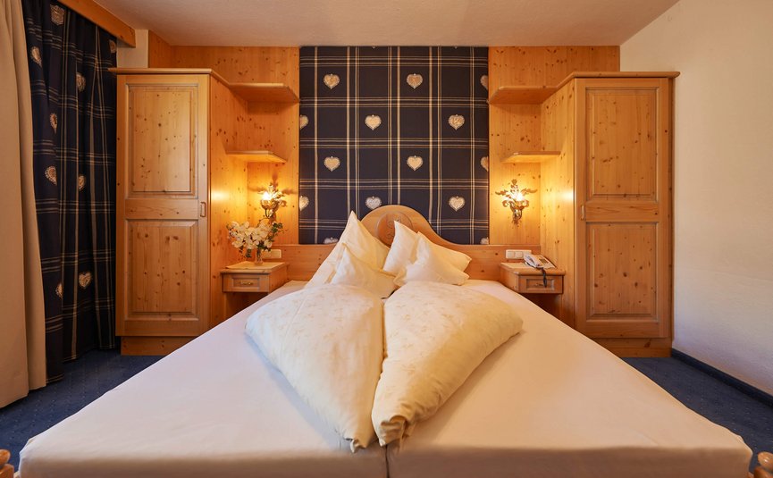 Alpenhotel Laurin ***S © studio22.at - Marcel Hagen Gemütliches Schlafzimmer mit Holzschränken und herzförmiger Bettdecke