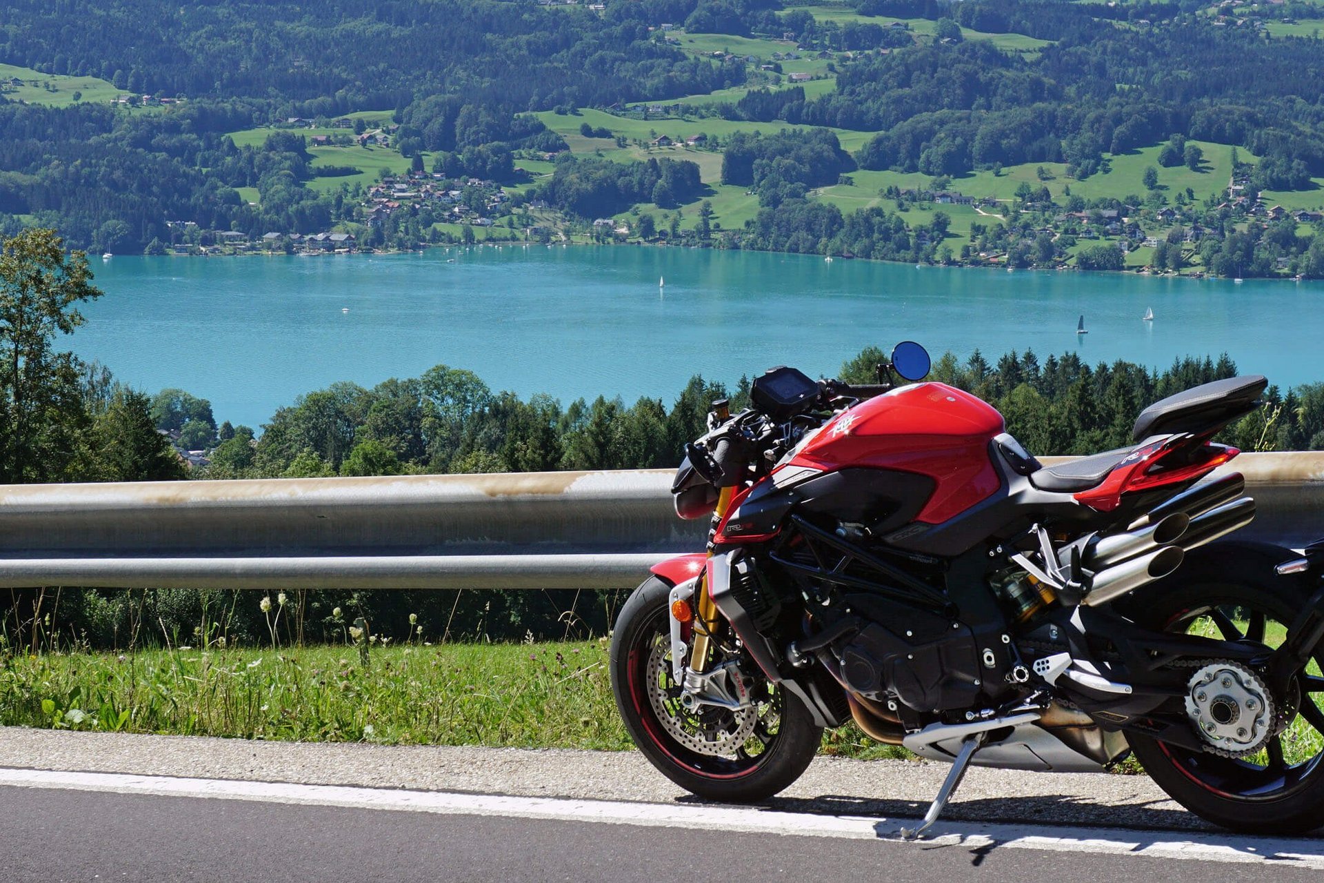 Motorradurlaub © Armin Hoyer Rotes Motorrad auf Bergstraße mit See und Hügeln im Hintergrund