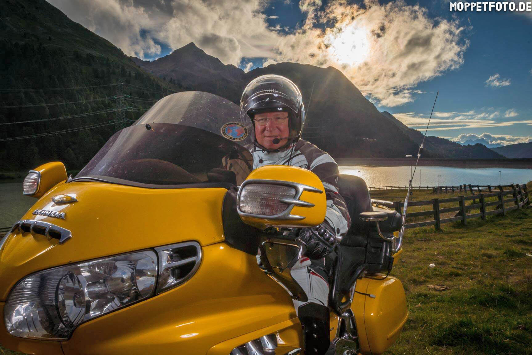 Motorradurlaub © Moppetfoto.de Mann auf gelbem Motorrad vor Berglandschaft bei Sonnenuntergang