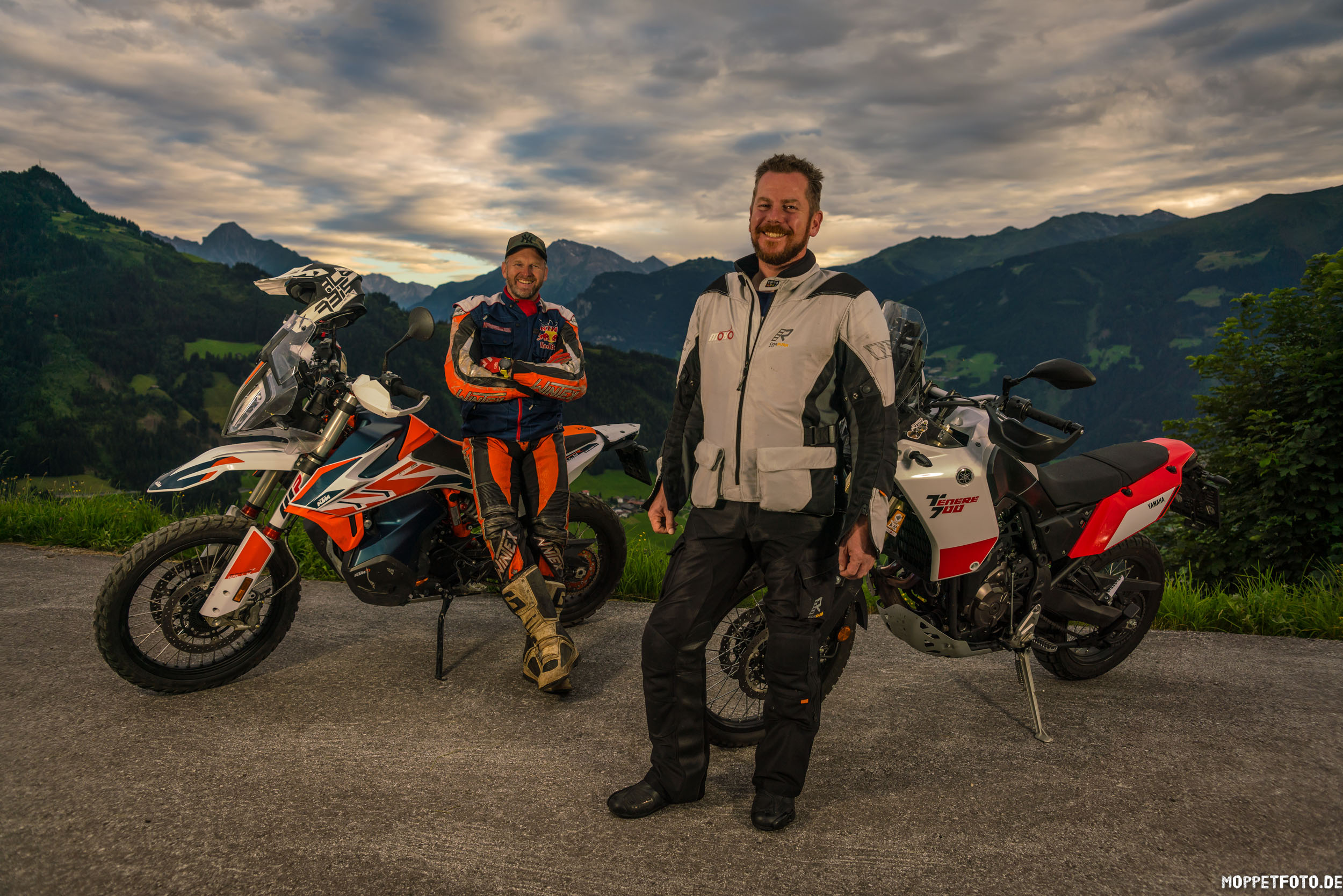 Motorradurlaub © Moppetfoto.de Zwei Motorradfahrer mit ihren Motorrädern vor bergiger Landschaft bei bewölktem Himmel