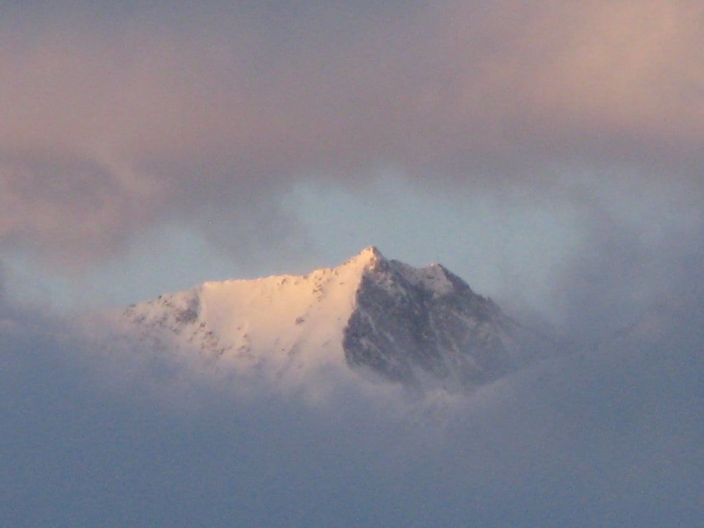 Weihnachtspauschale 7 Nächte Schneebedeckter Berggipfel umgeben von Wolken bei Sonnenuntergang