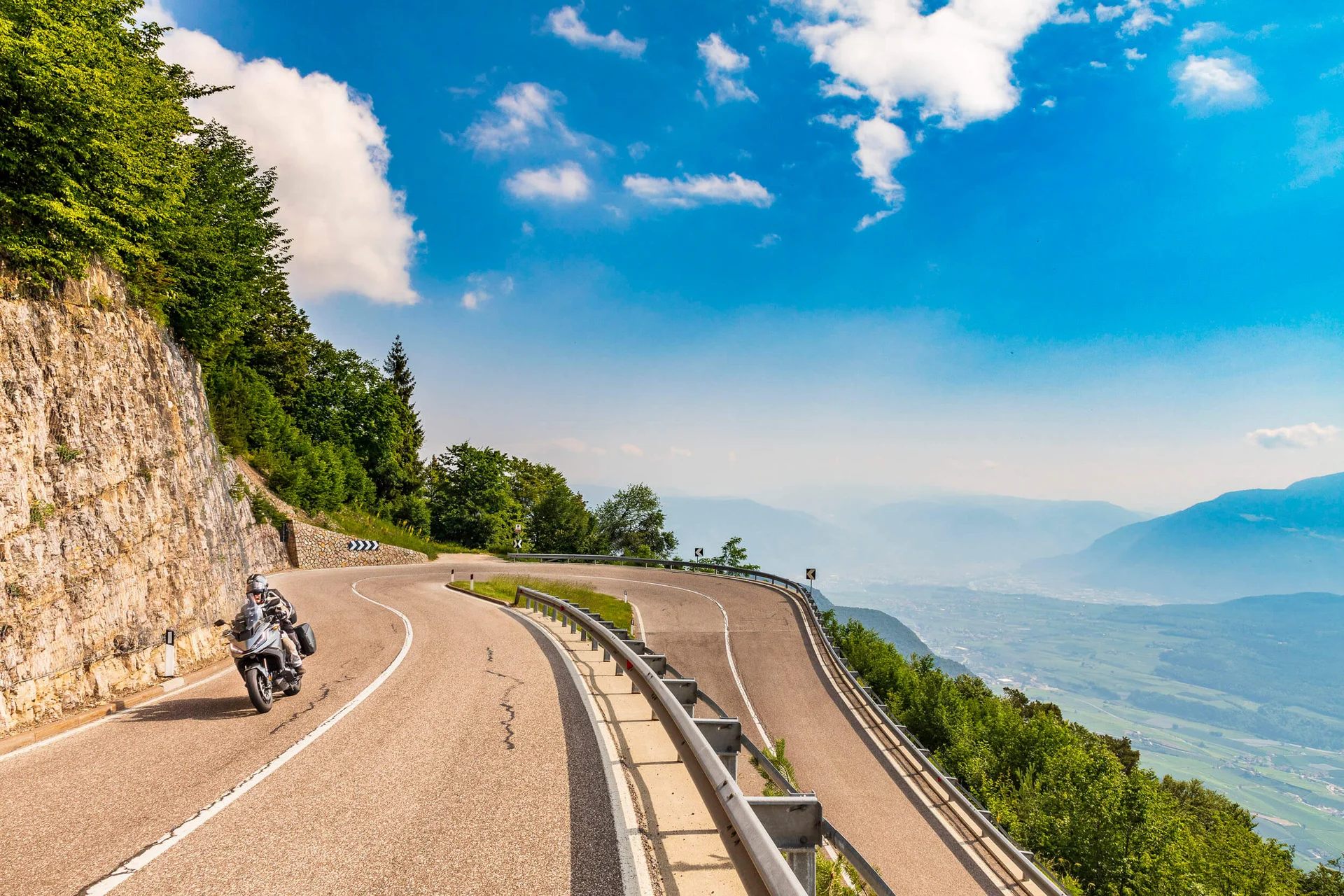 Motorbike holiday © Alexander Seger Motorcyclist on winding mountain road overlooking valley under clear sky