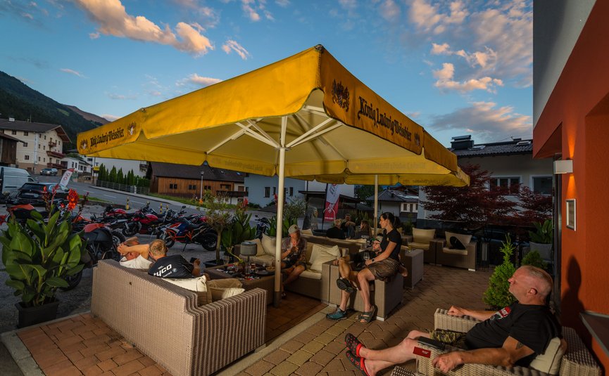 Hotel Sonnleiten *** © Moppetfoto.de People sitting under yellow umbrella on terrace near parked motorcycles