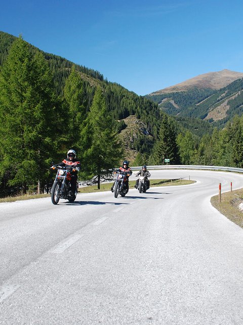 Motorradurlaub © Hotel Gasthof Strasswirt Drei Motorradfahrer fahren auf kurviger Bergstraße bei klarem Himmel