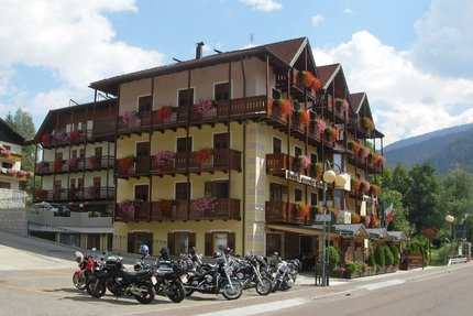 Hotel Monte Giner © Marisol s.n.c.di Pangrazzi Albino EC Multi-story hotel with flower balconies and motorcycles parked outside on sunny day