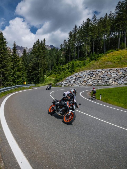 Motorradurlaub © Moppetfoto.de Motorradfahrer auf kurviger Bergstraße mit Fahrradfahrer und Wald