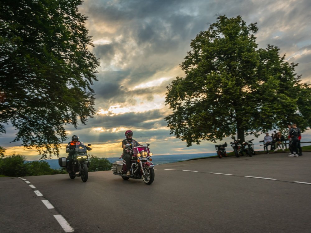 Motorradurlaub © Moppetfoto.de Zwei Motorradfahrer fahren bei Sonnenuntergang an einer Kurve vorbei.