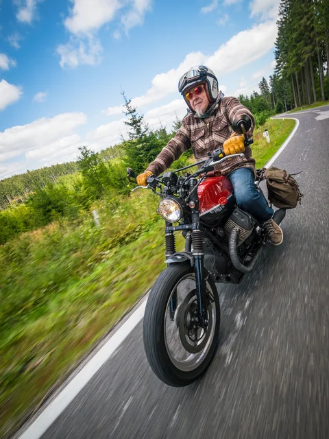 Motorradurlaub © Moppetfoto.de Älterer Mann auf Motorrad fährt kurvige Landstraße im Wald