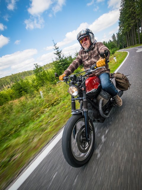 Motorradurlaub © Moppetfoto.de Älterer Mann auf Motorrad fährt kurvige Landstraße im Wald