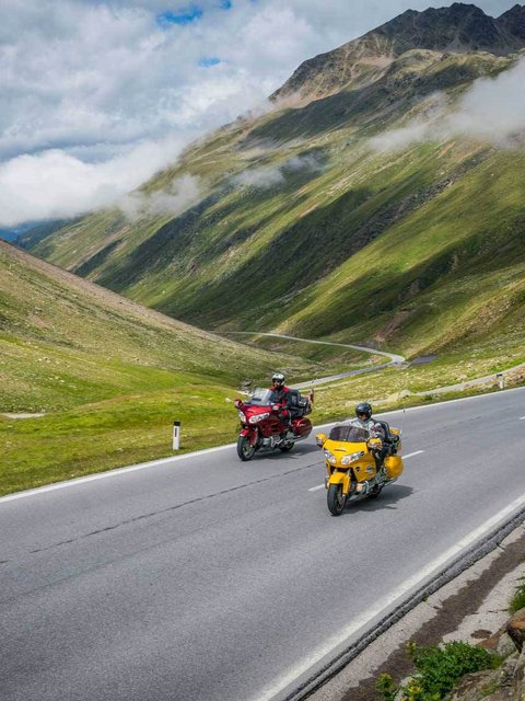 Motorradurlaub © Moppetfoto.de Zwei Motorräder fahren auf einer Bergstraße mit grünen Hügeln und Wolken