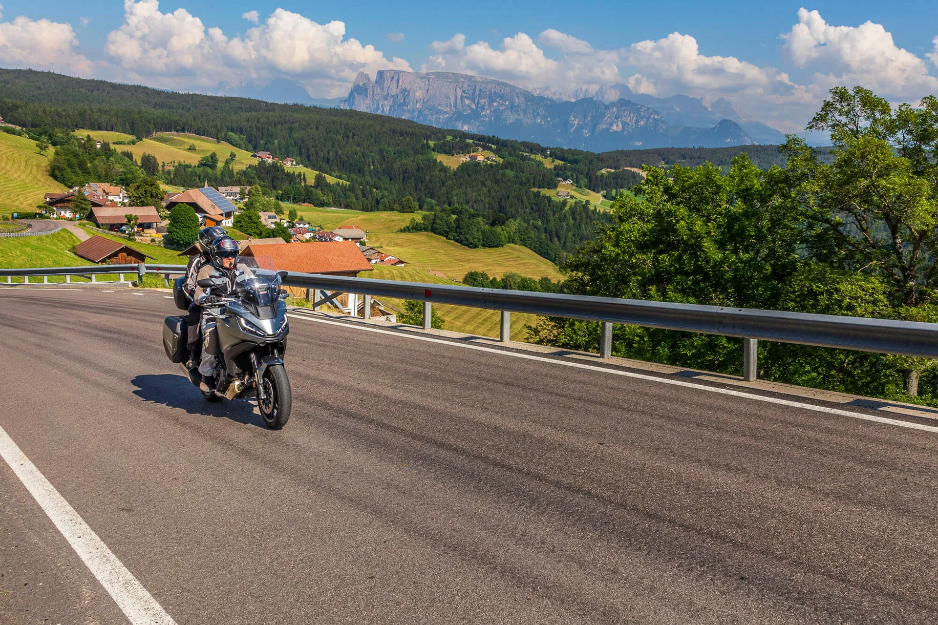Motorradurlaub © Alexander Seger Motorradfahrer auf kurviger Bergstraße mit Dorf und Bergen im Hintergrund