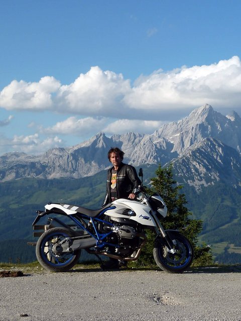 Motorradurlaub © Landhotel Gasthof Laudersbach Mann mit Motorrad vor Berglandschaft und blauem Himmel
