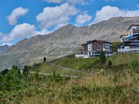 Alpenhotel Laurin © studio22.at - Marcel Hagen Alpine hotel on hillside with mountain backdrop and blue sky
