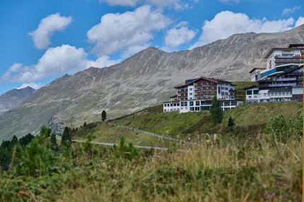 Alpenhotel Laurin © studio22.at - Marcel Hagen Alpine hotel on hillside with mountain backdrop and blue sky