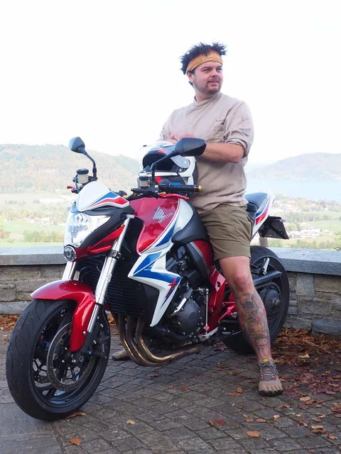 Motorradurlaub © Gast-Hof-Laden Schneeweiss Mann lehnt an rotem Motorrad mit Bergpanorama im Hintergrund