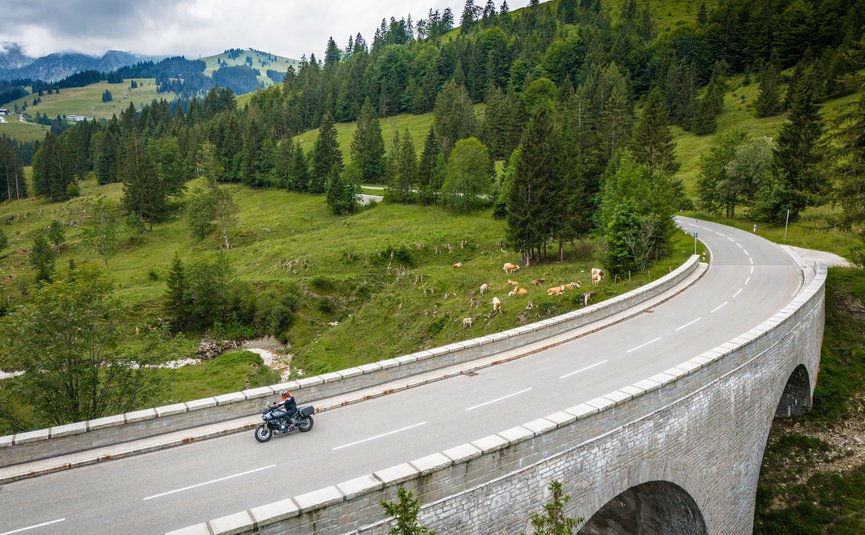 Gasthof Hotel Zur Post Samerberg *** © Moppetfoto.de Motorradfahrer auf einer Brücke in bergiger Landschaft mit Kühen und Tannen
