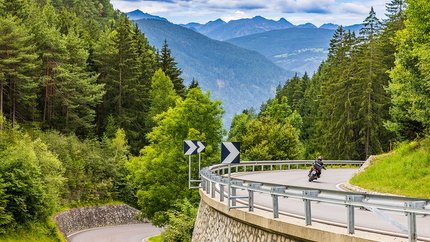 Südtirol - Dolomiten © Alexander Seger Motorradfahrer fährt auf kurviger Bergstraße im Wald