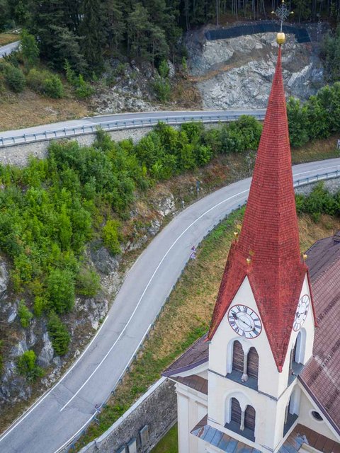 Motorradurlaub © Moppetfoto.de Kirchturm mit rotem Dach neben kurviger Bergstraße und Wald