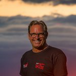 Motorvakantie in Beieren Man in zwart t-shirt lacht met rode zonsondergang op de achtergrond