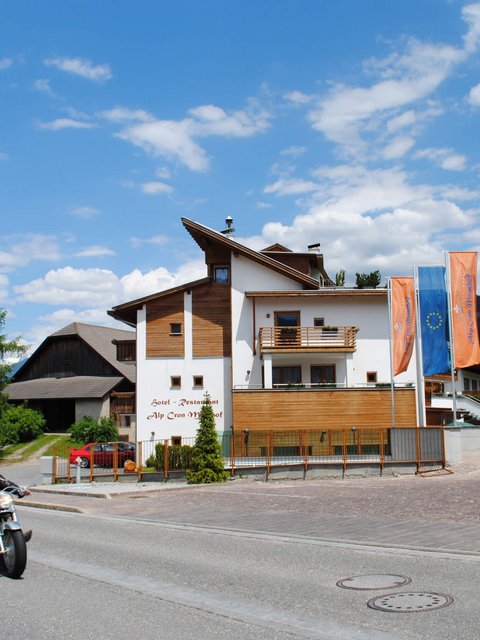 Motorradurlaub © Moar's Hotel in Olang Motorradfahrer fahren an einem Hotel in den Bergen bei sonnigem Wetter vorbei