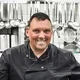 Motorradurlaub © Kreatur - Lechtaler Bergagentur Lächelnder Koch in schwarzer Uniform in professioneller Küche