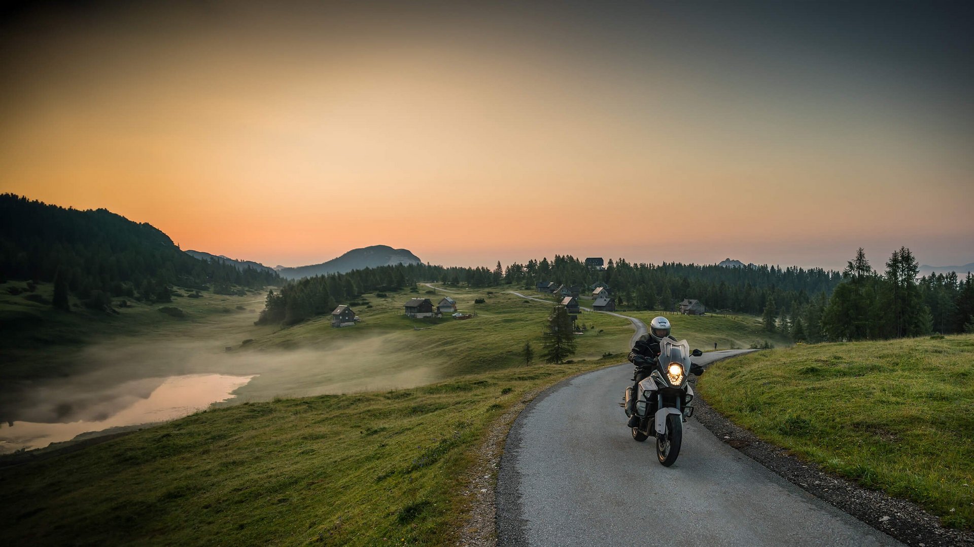 Motorradurlaub © Moppetfoto.de Motorradfahrer fährt auf Landstraße bei Sonnenuntergang mit Hütten und Bergen