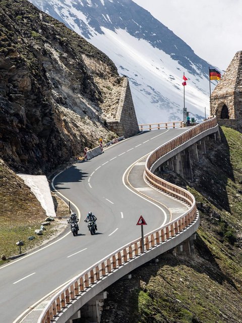 Motorradurlaub © Arturo Rivas Kurvige Bergstraße mit Motorradfahrern und historischen Grenzsteinen bei Schnee