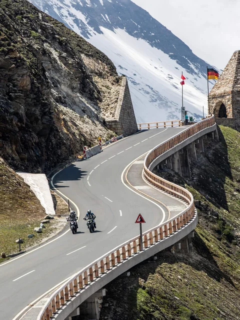 Motorradurlaub © Arturo Rivas Kurvige Bergstraße mit Motorradfahrern und historischen Grenzsteinen bei Schnee