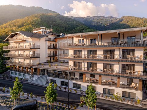 Cristallo Sport & Wellness Hotel © Andrea Acler Modern hotel building with balconies set against a forested mountain in sunlight