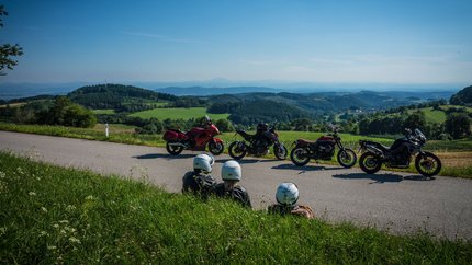 Niederösterreich © Moppetfoto.de Drei Motorradfahrer sitzen am Straßenrand mit Blick auf grüne Hügel und blaue Berge