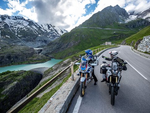 Großglockner – Hohe Tauern © Arturo Rivas Zwei Motorradfahrer auf Alpenstraße mit Bergsee und schneebedeckten Gipfeln