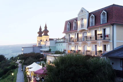 Hotel Rose © Hotel Rose Hotel building with lit balconies and twin-towered church in the background