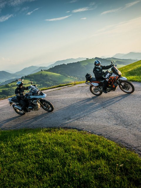 Motorradurlaub © Moppetfoto.de Zwei Motorradfahrer auf kurviger Bergstraße mit grünen Hügeln und blauem Himmel