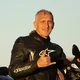 Motorradurlaub © Photo Matic Suc Mann im Leder-Motorradanzug gibt Handzeichen und steht neben Motorrad
