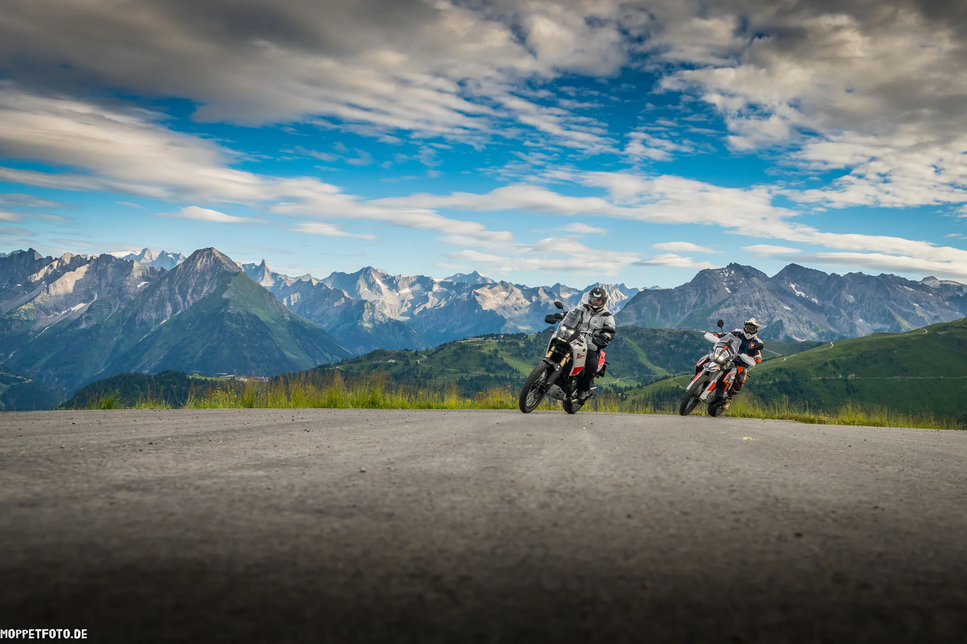 Motorradurlaub © Moppetfoto.de Zwei Motorradfahrer auf Bergstraße vor Alpenlandschaft unter bewölktem Himmel