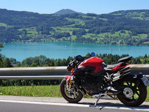 Attersee – Salzkammergut © Armin Hoyer Rotes Motorrad auf Bergstraße mit See und Hügeln im Hintergrund
