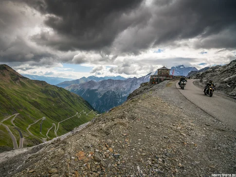 Lake Reschen - Stelvio Pass - Vinschgau Valley © Moppetfoto.de Motorcyclists on winding mountain road under dramatic cloudy sky
