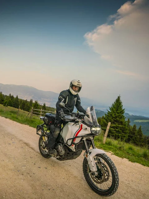 Motorradurlaub © Moppetfoto.de Motorradfahrer auf Schotterstraße in bergiger Landschaft mit Bäumen