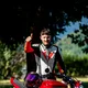 Motorradurlaub © Andrea Acler Mann mit Motorradkleidung zeigt Daumen hoch neben rotem Motorrad im Freien