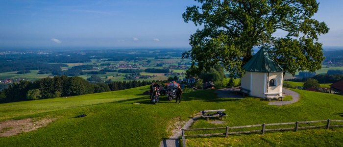 Motorvakantie in Beieren © Moppetfoto.de Heuvelachtig landschap met kapel, boom en mensen met scooters