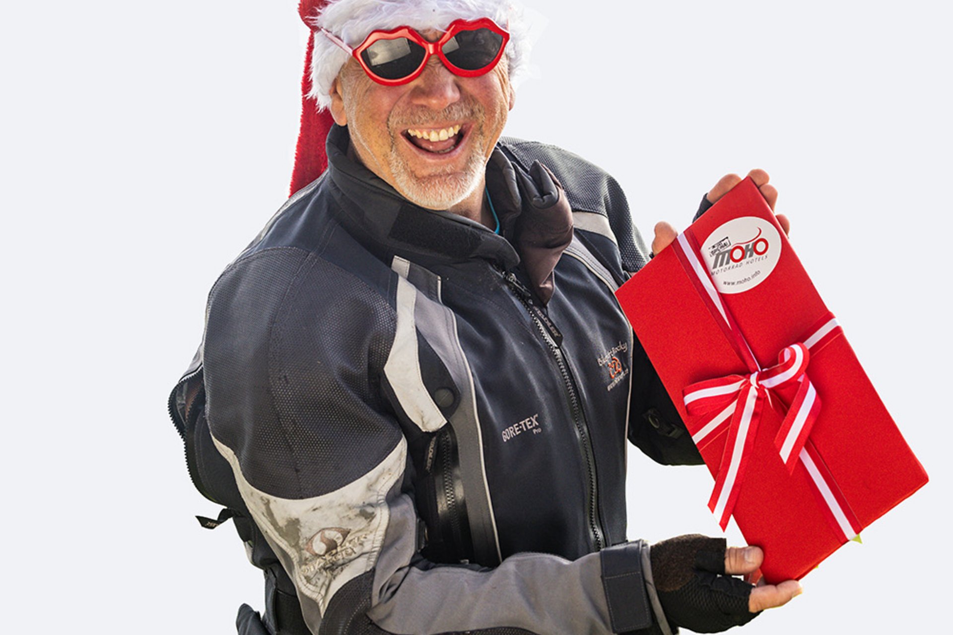 Motorradurlaub Mann im Motorradanzug mit Nikolausmütze hält rotes Geschenk mit Schleife